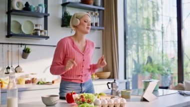Kaygısız sarışının tablet pişirme uygulaması sabah penceresinin yanında salata hazırlıyor. Kulaklıkla müzik dinleyen olumlu bir kadın vejetaryen yemeği yapıyor. Bayan sağlıklı kahvaltı rutinine konsantre oluyor. 