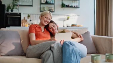 Tablet giyen kızlara sarılıp kanepede rahat rahat oturuyorlar. Gülümseyen sarışın esmer kadınlar hafta sonu bilgisayar uygulaması planlaması yapıyor. Mutlu lezbiyenler gülüyor. Teknolojiyle eğleniyorlar.