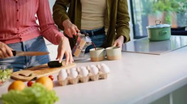 Ahşap mutfak yüzeyinde salatalık kesen yakın parmaklar. Neşeli arkadaşlar renkli salata yapıyorlar birlikte öğle yemeği hazırlıyorlar. Kahkaha atan kadın kahve fincanı getiriyor. Cep telefonundan selfie çeken iki kız.