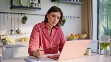 Ev mutfağındaki iş yerinde dizüstü bilgisayarla çalışan serbest çalışan bir bayan. Gülümseyen kadın muhasebeci bilgisayarını karıştırıyor. Uzaktan kumanda ofisinde mali rapor hazırlıyor. Mutfakta iş kadını düşünme görevi