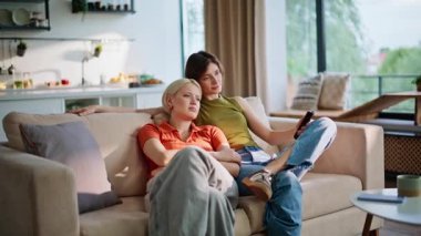 İki kız evde kanepede birlikte televizyon seyrediyor. Uzaktan kumandalı rahat kız arkadaşlar oturma odasında en sevdikleri programı seçiyorlar. Mutlu esmer kadın içeride kanal değiştiriyor.