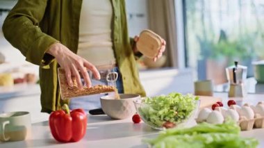 Kadın elleri mısır gevreği dolduruyor. Yakın çekimde süt ekliyor. Odaklanmış ev hanımı kahvaltı hazırlıyor tablet cihazında video değiştiriyor. Esmer kadın mutfakta sağlıklı yemek yiyor.