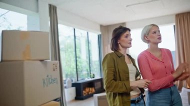 Rahibeler karton kutuların yakınındaki yeni oturma odasına bakıyor. Mutlu kadınlar birlikte apartman tasarımı hakkında konuşuyorlar. Gülümseyen genç aile modern gayrimenkullerde taşınmayı seviyor 