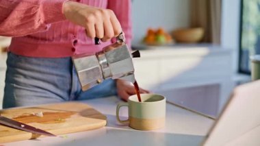 Kadın elleri mutfak tezgahında sabah kahvesini yudumlarken espresso dolduruyor. Kahvaltını yapan gülümseyen sarışın kadın sıcak mutfağın tabletinde videolar izliyor. Rahat kız sıcak içeceğini yudumluyor.