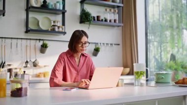 Serbest çalışan bir kadın mutfaktaki yakın planda bilgisayardan e-posta yazıyor. Odaklanmış ev hanımı, mutfakta çalışan bilgisayar klavyesine mesaj atıyor. Uzaktan çalışan bayan cep telefonunu arıyor.