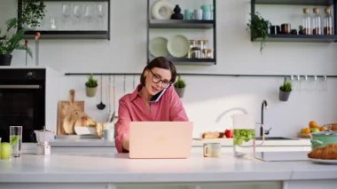 Neşeli internet yöneticisi cep telefonunu arıyor. Ev ofisini kapatıyor. Mutfakta elinde kahve fincanı tutan pozitif bir iş kadını. Kadın serbest çalışan telefonda müşteri konuşuyor. 