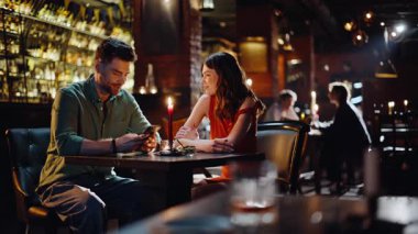 Barda oturmuş gülümseyen romantik bir çift. Sevgi dolu bir çift, karanlıkta oturup mum yakmayı tartışıyor. İki mutlu insan, gece kulübünde güzel vakit geçiriyorlar..