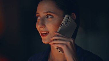 Kadın çalışanı aramak, gece ofisinde sipariş vermek, yakın plan. Portre gülümseyen iş kadını, karanlık bir evde akıllı telefondan konuşuyor. Mutlu esmer, cep telefonu konuşmalarında iş konuşuyor..