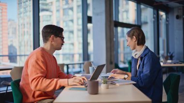 Takım arkadaşları modern kafe açık alanda iş projesinde çalışıyor. Dizüstü bilgisayar yazan bıyıklı adama kağıt veren gülümseyen kadın. Ofiste ortak çalışarak pazarlama stratejisi planlayan iki takım üyesi.