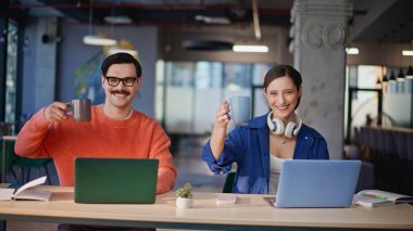 Gülümseyen takım, yaratıcı ajansın çalışma alanına yakın çekim yaparken elinde bardak içeceği tutuyor. Neşeli meslektaşlar modern ofiste kahve molası veriyorlar. Mutlu şirket çalışanları çevrimiçi işten dinleniyor..