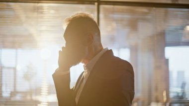 Siluet gergin direktörü cep telefonunu arıyor ve akşam vakti güneş ışığı koridorunu kapatıyor. Koridordaki akıllı telefonda tartışan öfkeli yaşlı iş adamı. Yetişkin yönetici telefonda bağırıyor.