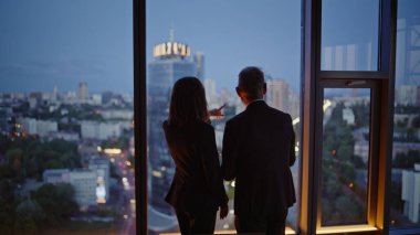 Ofis çalışanları panoramik pencereden şehir manzarası izliyorlar. Karanlık şehir ufkunun keyfini çıkaran iki iş arkadaşı dik iş gökdeleninin arkasında. Şirket ortakları şirket işbirliğini tartışıyor.