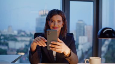 Rahat yönetici cep telefonunu akşam iş yerinde kapatıyor. Gülümseyen iş kadını akıllı telefon mesajları okuyor ve ofis işlerine ara veriyor. Zarif kadın yönetici telefon bankacılığı uygulamasına göz atıyor.