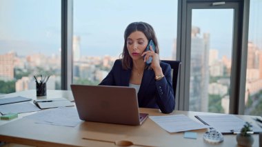Modern iş yerinde akıllı telefondan konuşan, dizüstü bilgisayarı olan çok görevli bir kadın. Kendine güvenen bir iş kadını cep telefonuyla iş görüşmelerini tartışıyor. Ciddi bayan patron, müzakere ortaklarını arıyor..