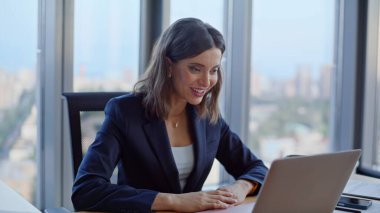 Modern ofiste online toplantıdan başlayarak dizüstü bilgisayarlı web kamerasıyla gülümseyen bir yönetici selamlıyor. Hevesli iş kadını iş yerinden el sallıyor. Mutlu bayan sanal konferansın tadını çıkarın..