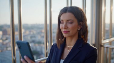 Yakın plan esmer, cep telefonu bankacılığı uygulaması ofis balkonunda. Portre başarılı iş kadını yüksek binadaki cep telefonu mesajını okuyor. Zarif kadın çalışan akıllı telefon gibi görünüyor..