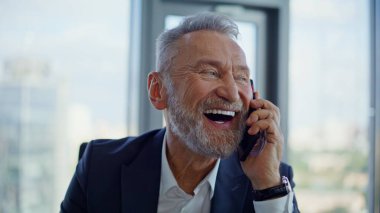 Neşeli, yaşlı CEO 'nun cep telefonunu araması iş ortaklığı başarısını aydınlık ofis kapanışında gösteriyor. Portre mutlu iş adamı konuşan akıllı telefon. Gülümseyen sakallı menajer telefonda harika haberleri tartışıyor..