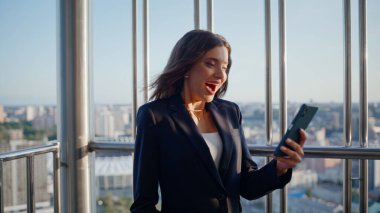 Ofis balkonunda sevinç dolu mesajlar alan şaşırtıcı bir çalışan. Cep telefonuna bakan aşırı neşeli iş kadını evet hareketi yapıyor. Gülümseyen esmer, başarıya duygusal tepki veriyor..