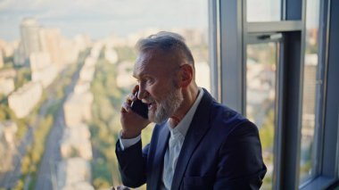 Yüksek katlı bir iş merkezinde deneyimli bir danışman cep telefonuyla konuşuyor. Gülümseyen kıdemli işadamı ofisin panoramik penceresinde cep telefonunu arıyor. Neşeli avukat telefonla işi tartıştı.