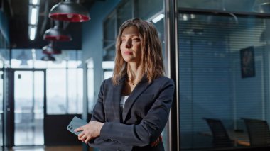 Resmi takım elbiseli kadın şirket binası koridorunu kapatıyor. Ofiste cep telefonu tutan düşünceli bir iş kadını. Kendine güvenen yönetici kadın koridorda iş düşünüyor..