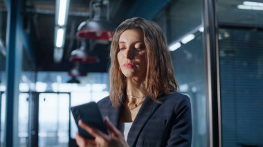 Heyecanlı yönetici modern şirket lobisinde cep telefonuna bakıyor. Gülümseyen iş kadını ofis koridorunda akıllı telefon tutarak kazandığına şaşırdı. Duygulu bayan salonda evet jesti yapıyor..