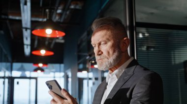 Ofis binası koridorunda cep telefonunu izleyen kıdemli girişimci. Somurtkan yaşlı işadamı koridorda cep telefonu mesajı okuyor. Ciddi bir işletme sahibi kapalı alanda akıllı telefonla e-posta gönderiyor