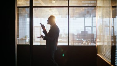 Müdür cep telefonu hoparlöründen konuşuyor. Gün batımını kapatıyorum. Siluet kıdemli işadamı koridordaki akıllı telefon sesli mesajını kaydediyor. Olgun yönetici cep telefonuyla dikte ediyor.