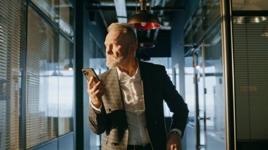 Endişeli profesyonel görünümlü cep telefonu ekranı ofis koridorunda duruyor. Gergin kıdemli işadamı koridorda e-posta okurken endişeli bir sorun yaşıyor. Salondaki akıllı telefon mesajında sakallı yönetici düşüncesi.