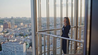 Gülümseyen iş kadını modern balkon binasından arıyor. Başarılı kadın girişimci cep telefonuyla konuşuyor ofis dışında iyi haberleri paylaşıyor. Zarif bayan yönetici akıllı telefon konuşuyor..