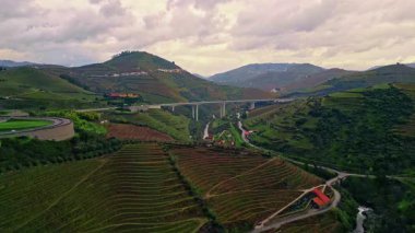 Hillside fields create layered geometric landscape. Small river flowing calmly between agricultural terraces. Cozy settlements scattered on mountain ridges. Rural farms stand in vast countryside.