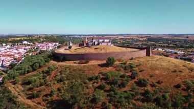 Aerial view old fortress rising above quiet Portugal village. Stone wall surrounding chapel on arid terrain. Beautiful heritage landscape with cultural landmark. Historical monument standing on hill.