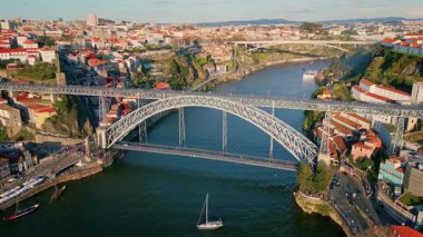 Drone view bridge over Douro river in Porto with sailing beautiful yachts. Steel arch symbol rising above water linking Portugal city banks. Monumental landmark of Dom Luis connecting town districts.