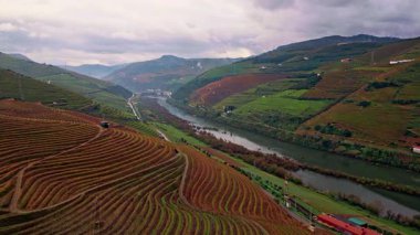 Breathtaking green slopes panorama under gloomy cloudy sky. Terraced agricultural fields covering hills aerial view. Small calm river running through hillside greenery. Beautiful rural landscape.