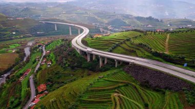 Highway bridge crossing terraced fields in mountain valley. Drone view transport line above rural landscape with river and houses. Green hills showing connection road and nature. Countryside scenery