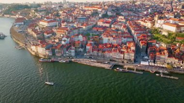 Coastal Portugal city standing on river beautiful sunny day drone view. Cozy residential district with tiled roof buildings placed on coast. Small boats floating in green water. Urban architecture.