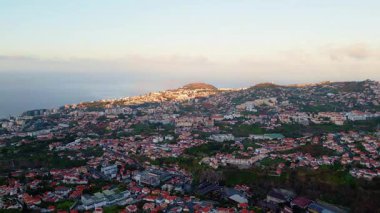 Aerial panorama hillside town with red rooftops. Urban pattern cozy Mediterranean settlement at summer evening. Drone view residential districts surrounded greenery. Scenic traditional city structure.
