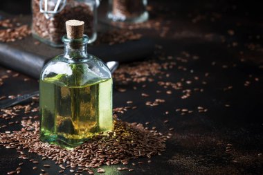 Linseed or flax oil in glass bottle and seeds, dark background, selective focus clipart