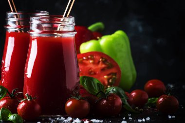 Sağlıklı ve kullanışlı baharatlı smoothies veya suyu kırmızı domates ve biber cam şişelerde karanlık bir arka plan, seçici odak üzerinde yeşil fesleğen ile