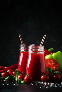Sağlıklı ve kullanışlı baharatlı smoothies veya suyu kırmızı domates ve biber cam şişelerde karanlık bir arka plan, seçici odak üzerinde yeşil fesleğen ile