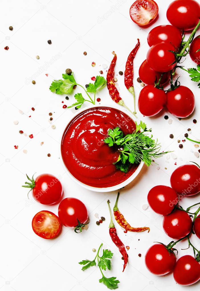 Spicy tomato ketchup sauce with herbs, chili and cherry tomatoes in bowl on white food background, top view