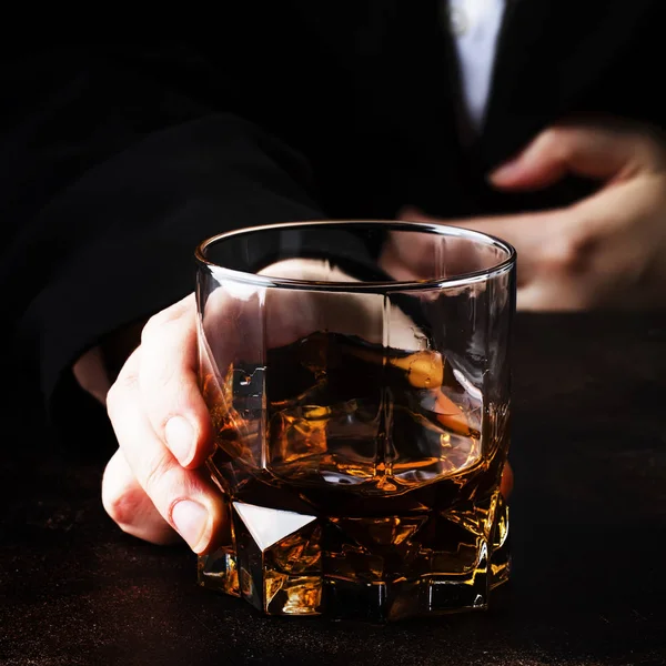 Glass with whiskey in hand, dark background, selective focus