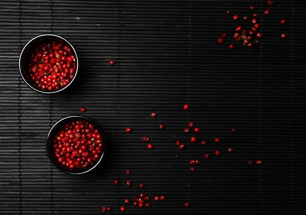 Pink rose pepper in bowl, black background, top view