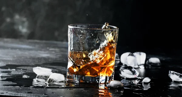 Whiskey with ice, splashes out of glass, dark background, selective focus
