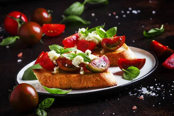 Italian crispy toasted bruschetta with black and brown cherry tomatoes, blue cheese and basil, selective focus
