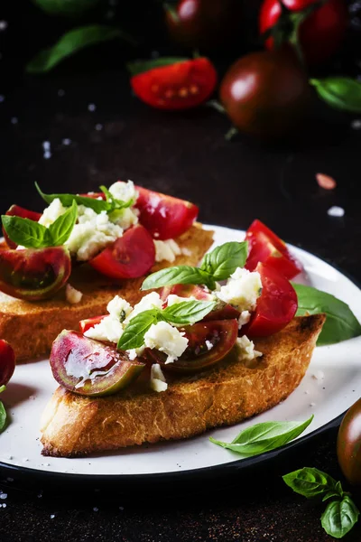 Italian crispy toasted bruschetta with black and brown cherry tomatoes, blue cheese and basil