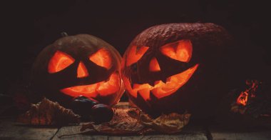 İki Halloween balkabağı Jack-o-Lantern düşen yapraklar ve alevler koyu ahşap zemin üzerine