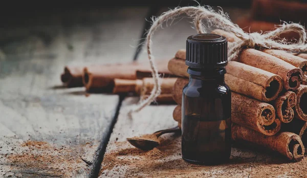 Essential cinnamon oil in a small bottle, ground cinnamon and cinnamon sticks on old wooden background