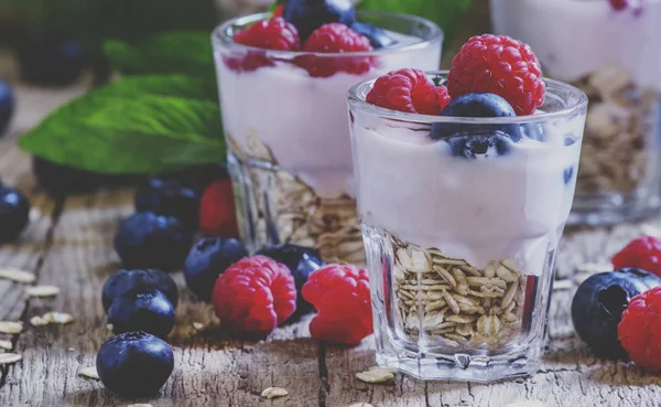 Sweet berry dessert with oatmeal, yogurt, blueberries and raspberries, vintage wooden background