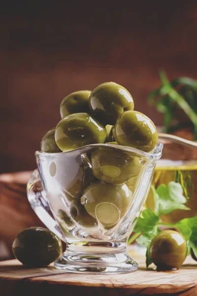 Green greek olives in glass bowl on the vintage wooden background