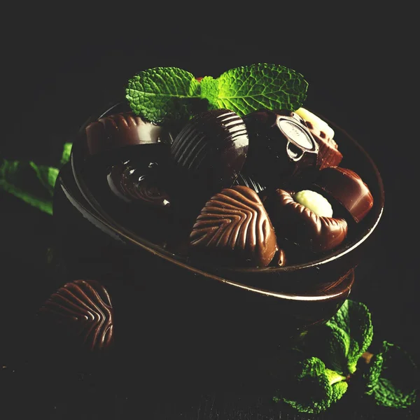 Chocolate candies, assorted, decorated with mint leaves, dark background